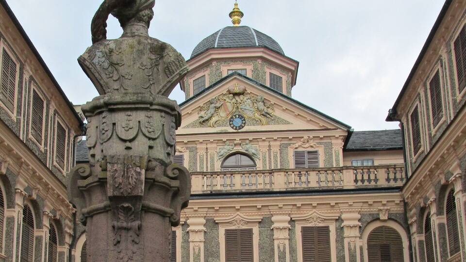 A historic building with ornate architecture, including a clock and a statue on a column.