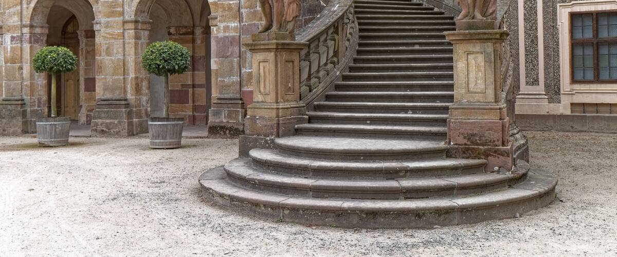 A grand staircase with ornate balustrades and statues, leading to a building with classical architecture.
