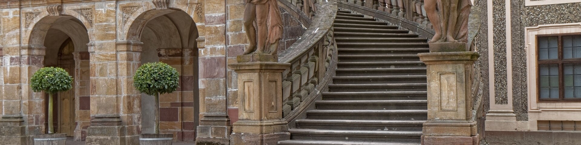 A grand staircase with ornate balustrades and statues, leading to a building with classical architecture.
