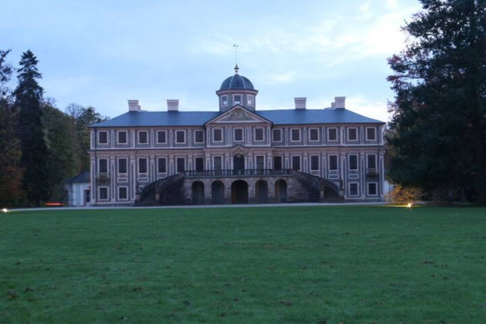 Ein großes, klassizistisches Gebäude mit einer zentralen Kuppel und symmetrischer Architektur, umgeben von einem gepflegten Rasen.