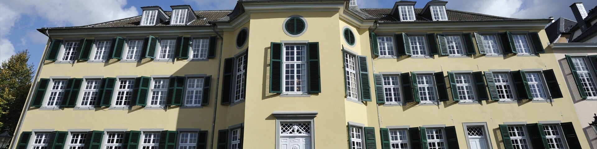 A large yellow building with green shutters and a clock tower.