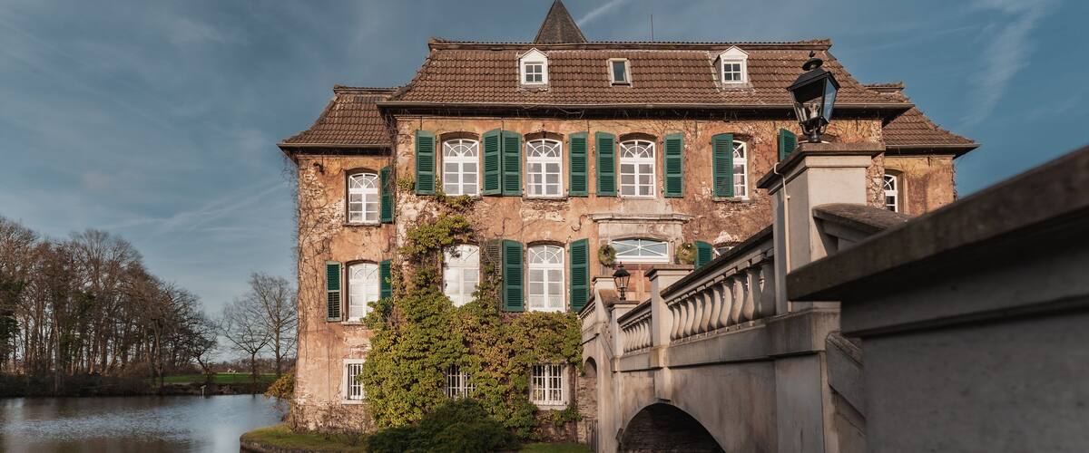 A historic building with green shutters, a bridge, and a calm river.
