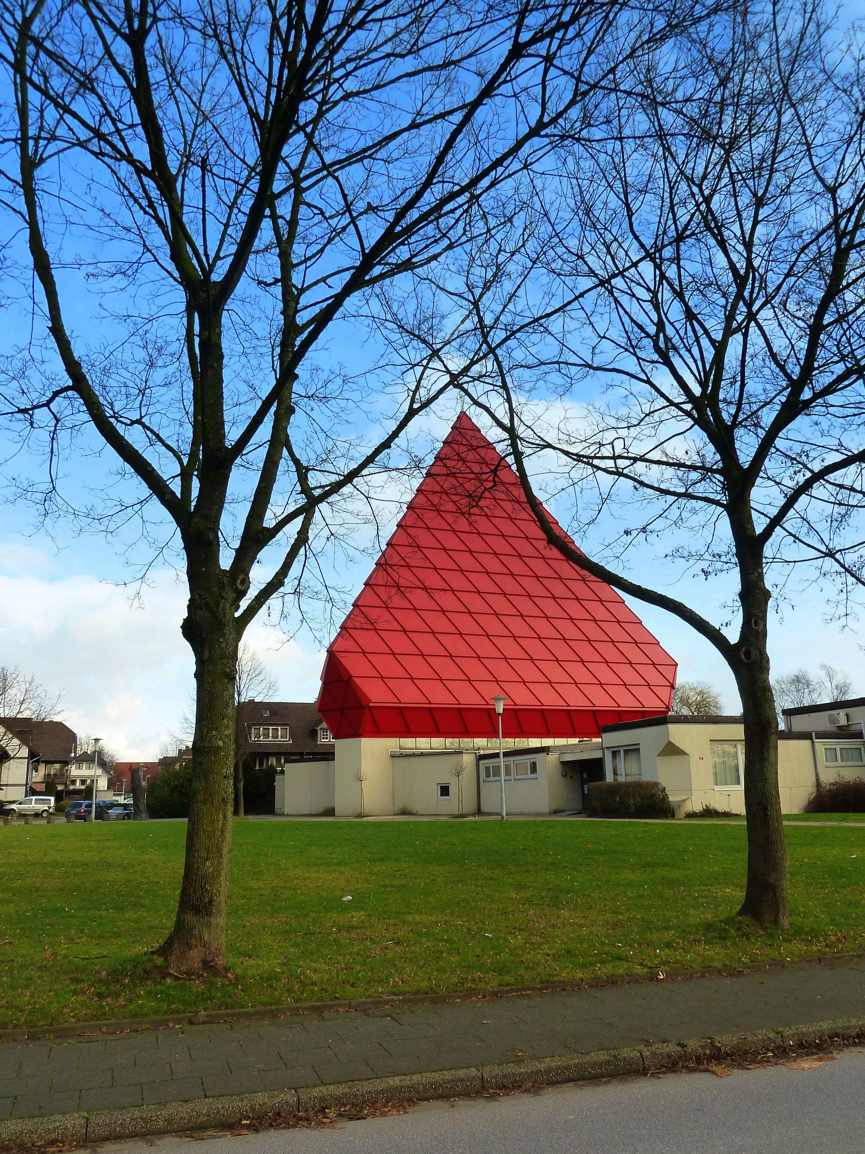 A red pyramid-shaped building with a flat roof, surrounded by trees and a grassy area.