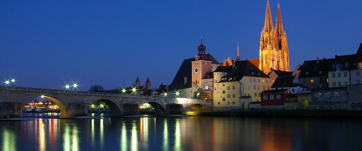 The Stone Bridge in Regensburg over the Danube at sunset with the Regensburg Cathedral in the background.