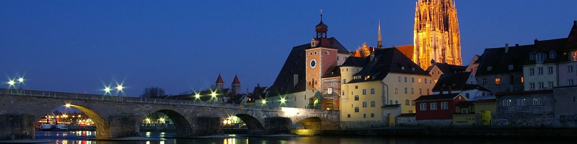 The Stone Bridge in Regensburg over the Danube at sunset with the Regensburg Cathedral in the background.