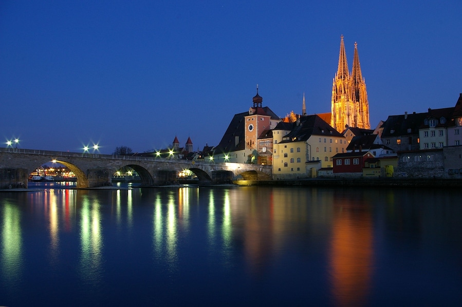 The Stone Bridge in Regensburg over the Danube at sunset with the Regensburg Cathedral in the background.