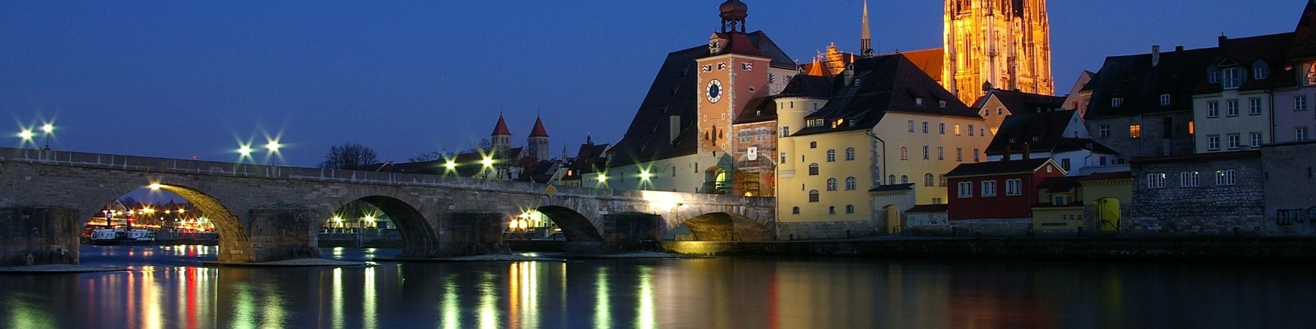 The Stone Bridge in Regensburg over the Danube at sunset with the Regensburg Cathedral in the background.