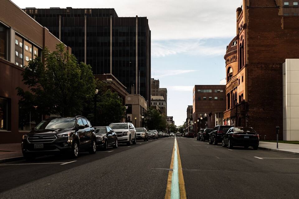 A city street lined with parked cars and tall buildings.