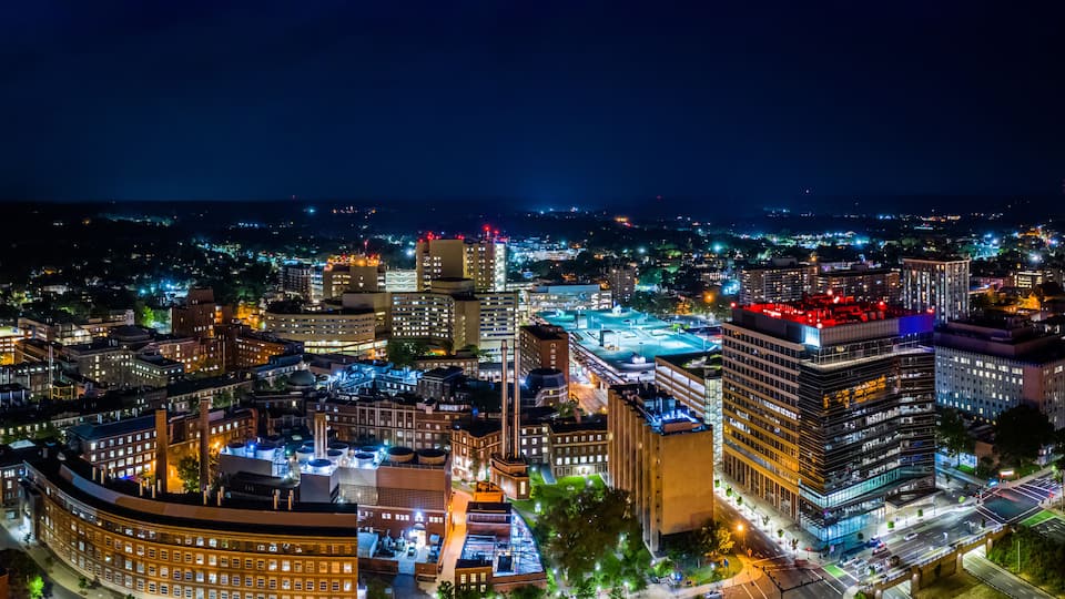 A nighttime cityscape with illuminated buildings and a river.