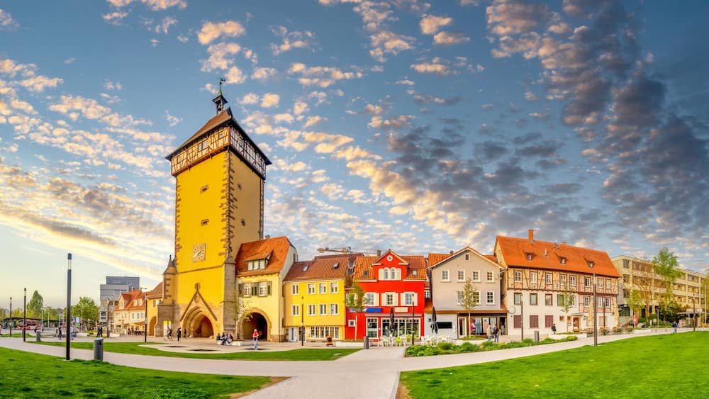 A historic town square with a prominent yellow tower, colorful buildings, and a clear sky.