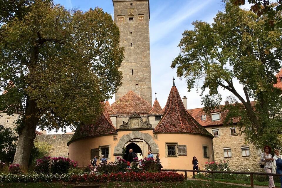 Um edifício histórico com uma torre alta, rodeado por árvores e um jardim bem cuidado.