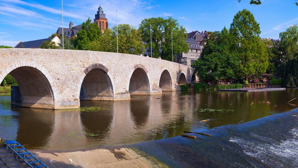 A stone bridge over a river with a town in the background.