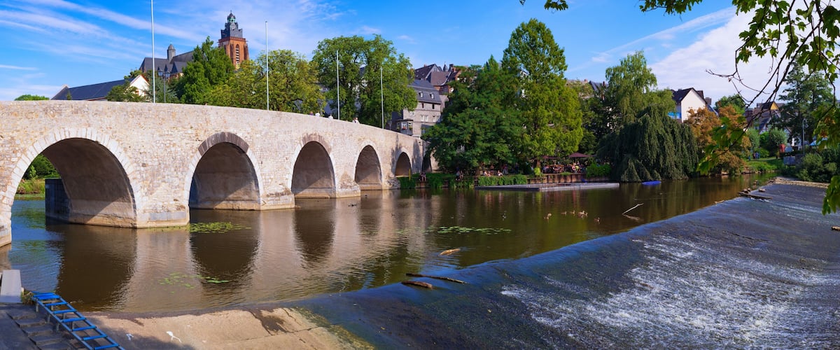 A stone bridge over a river with a town in the background.