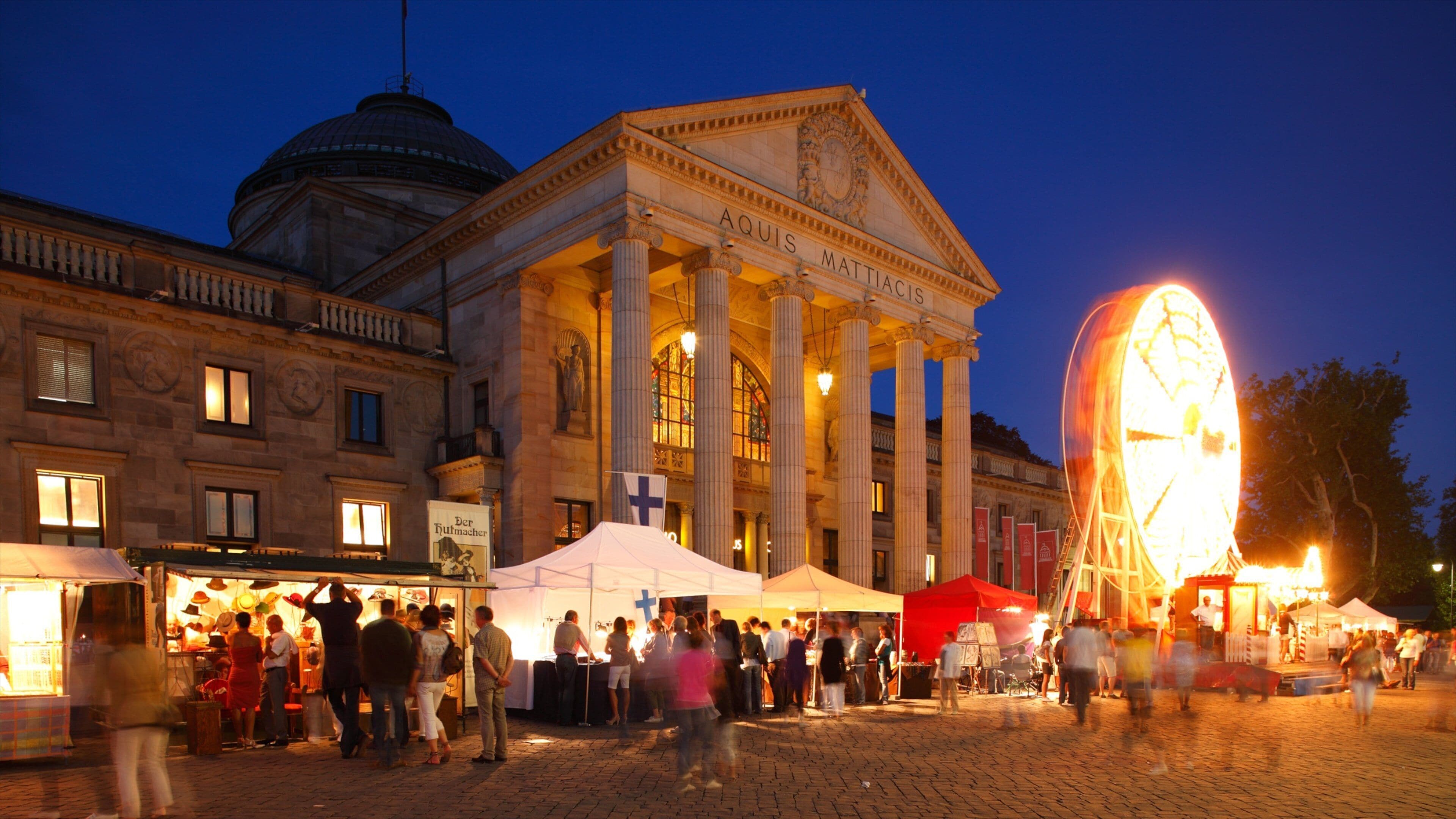 A historic building with columns and a dome, surrounded by a crowd and market stalls.