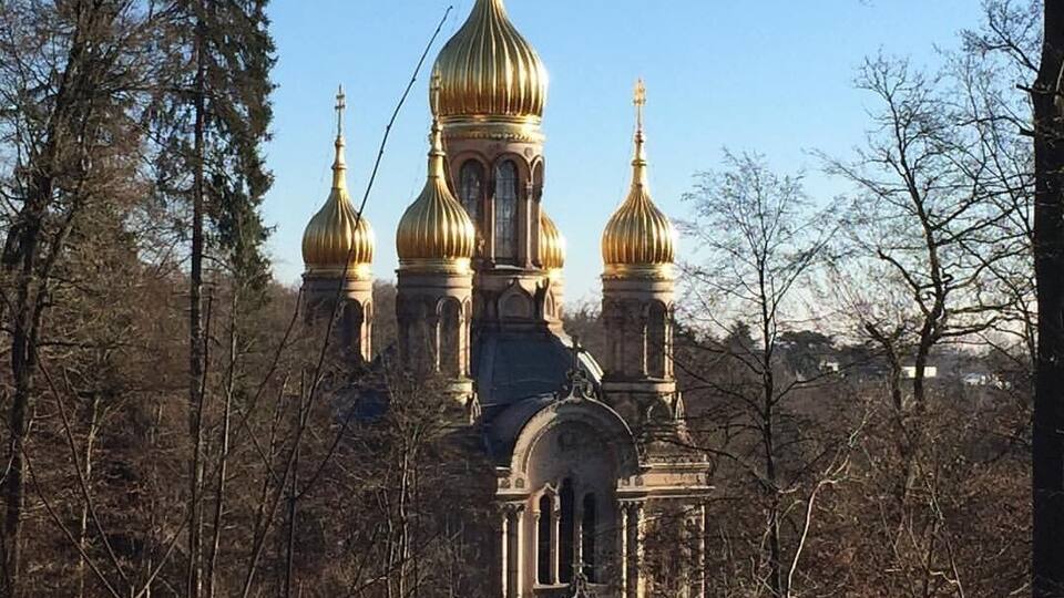 A historic church with golden domes surrounded by trees.