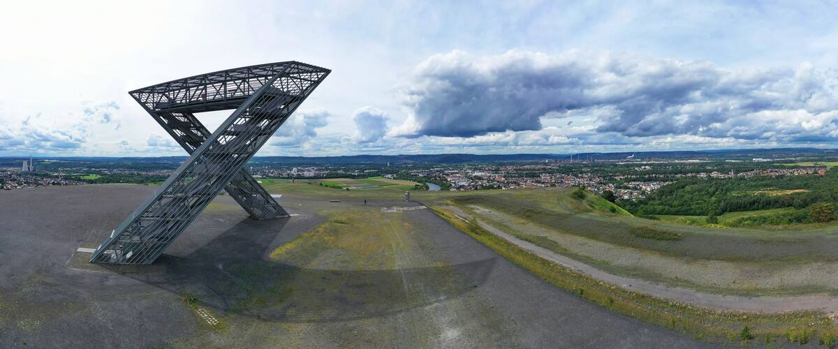 A large metal structure in an open field with a town and hills in the background.