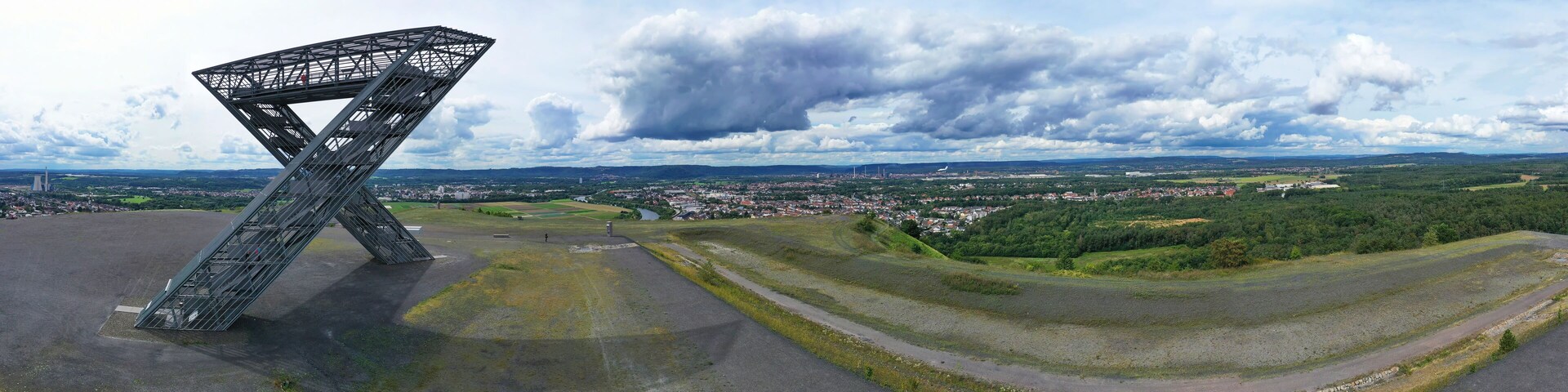A large metal structure in an open field with a town and hills in the background.