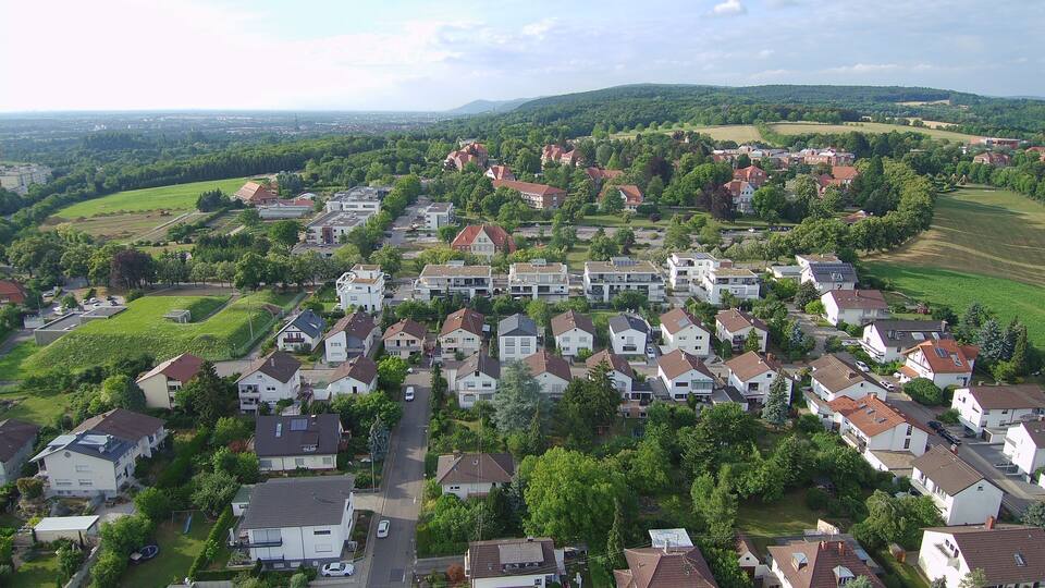 A residential area with houses, green fields, and a distant cityscape.
