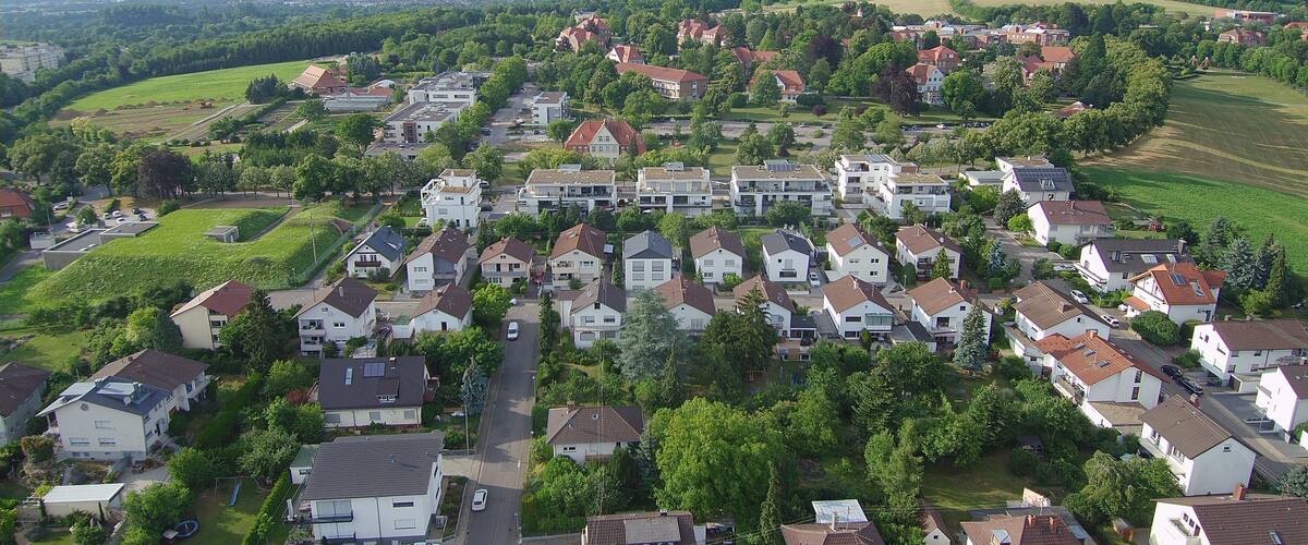 A residential area with houses, green fields, and a distant cityscape.