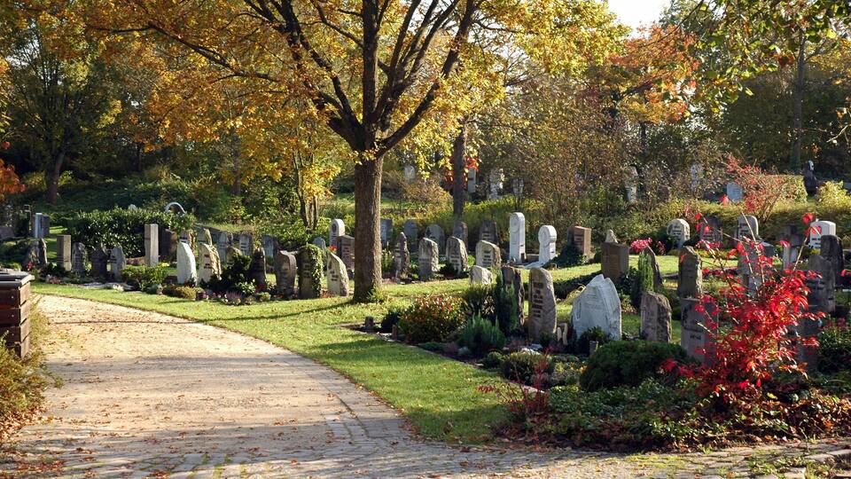 A cemetery with stone headstones, a pathway, and autumn foliage.