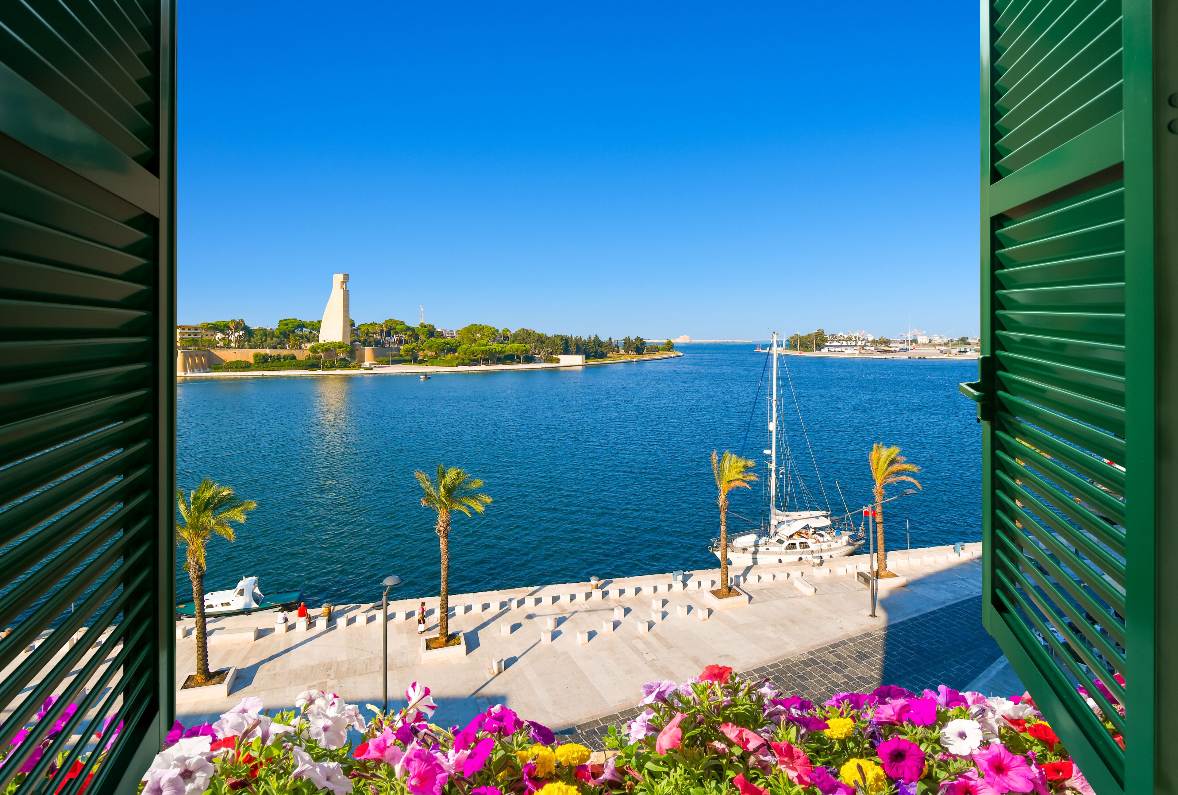 A coastal view with a clear blue sea, a white lighthouse, and a green railing.