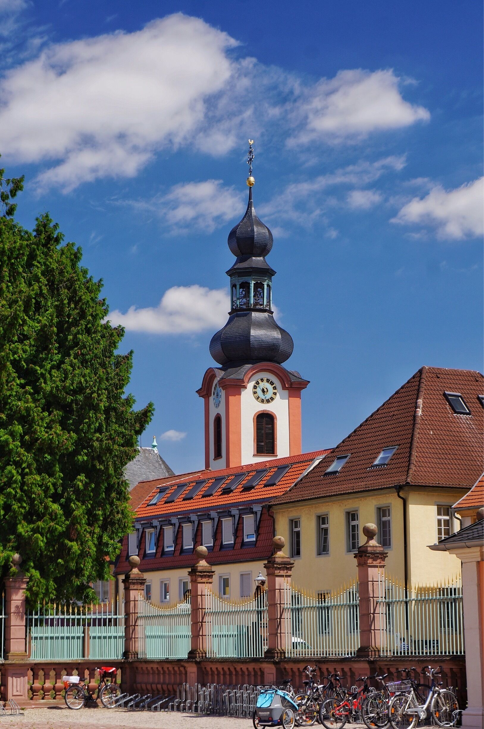 A church with a clock tower, a fence, and bicycles parked in front.