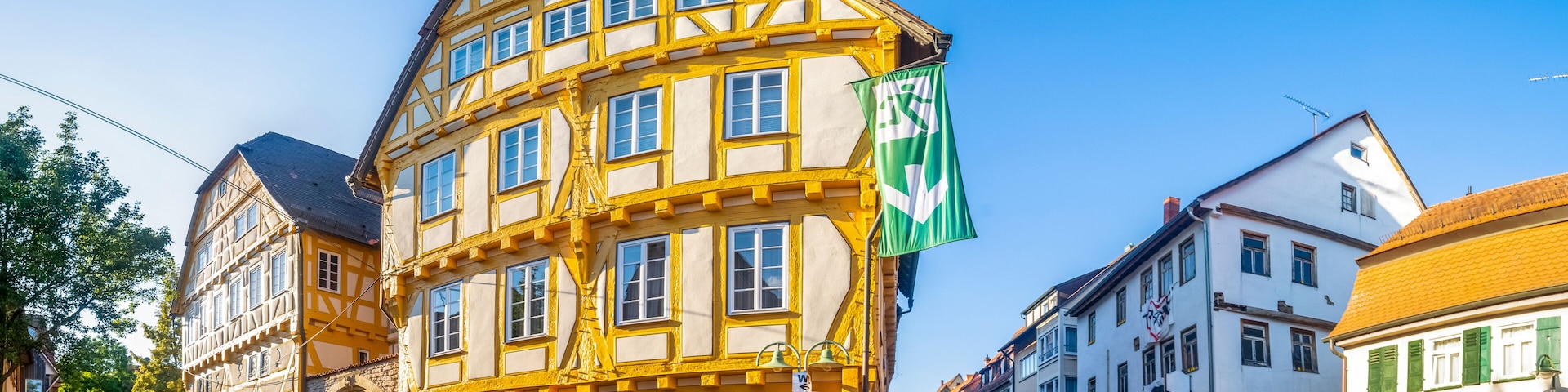 A historic yellow and white building with a clock, cobblestone street, and European flags.