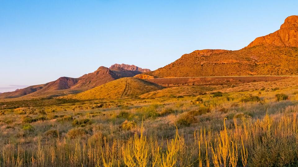 A desert landscape with a prominent mountain range and a train track.