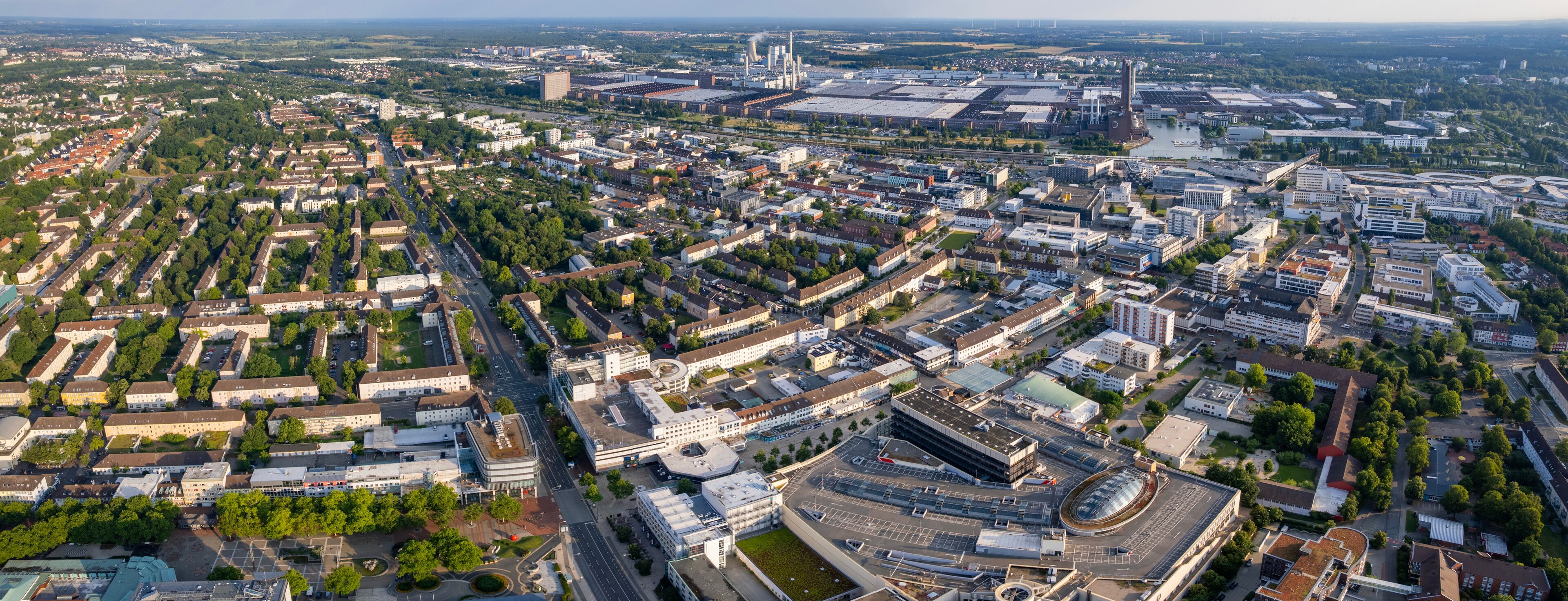 Vista aérea de uma cidade com intenso desenvolvimento urbano, incluindo uma mistura de edifícios residenciais e comerciais, uma grande área industrial e um complexo de edifícios circulares de destaque.