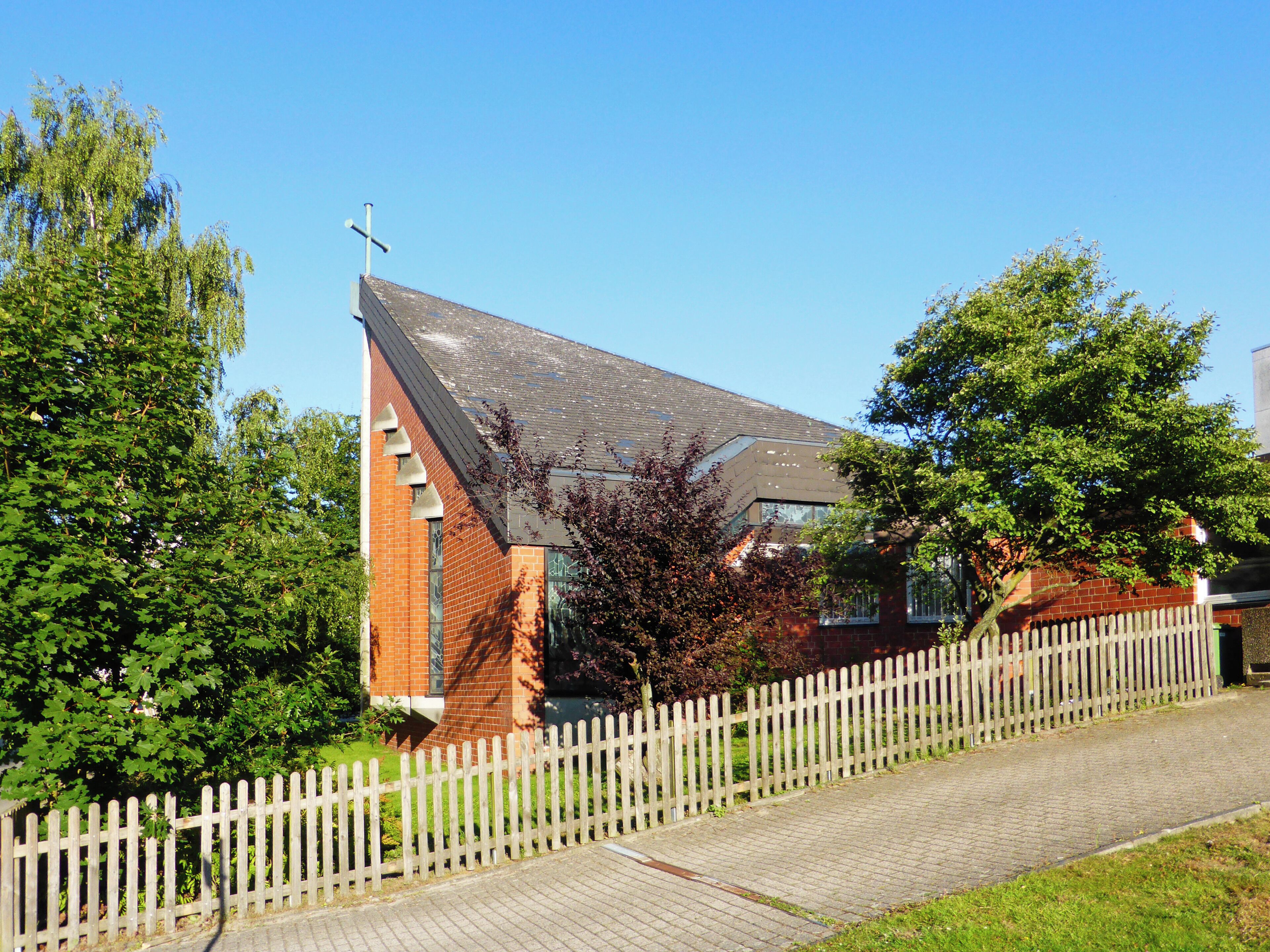 A church with a white fence, surrounded by trees and greenery.