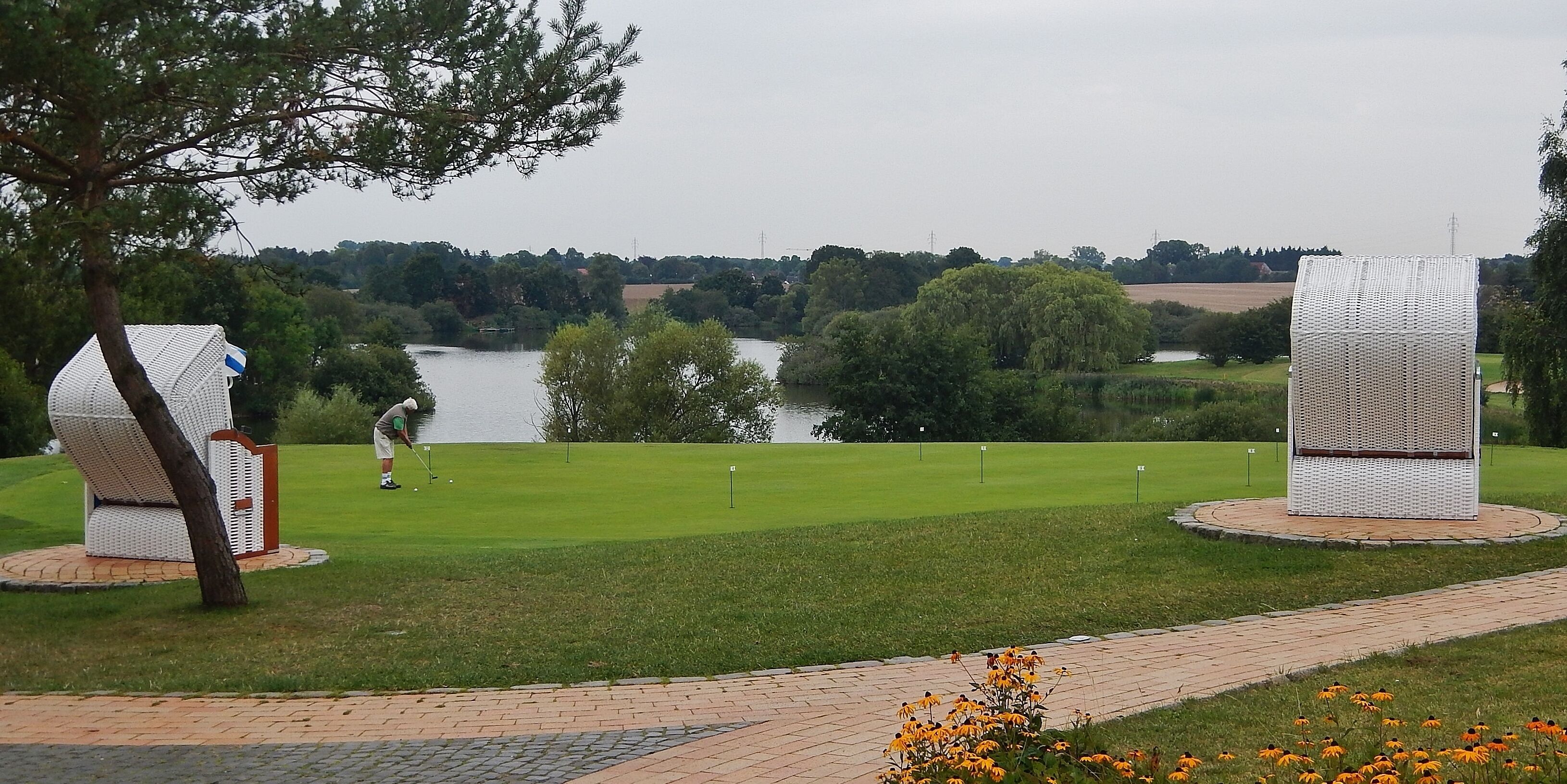 A golf course with a lake, trees, and a sculpture in the foreground.