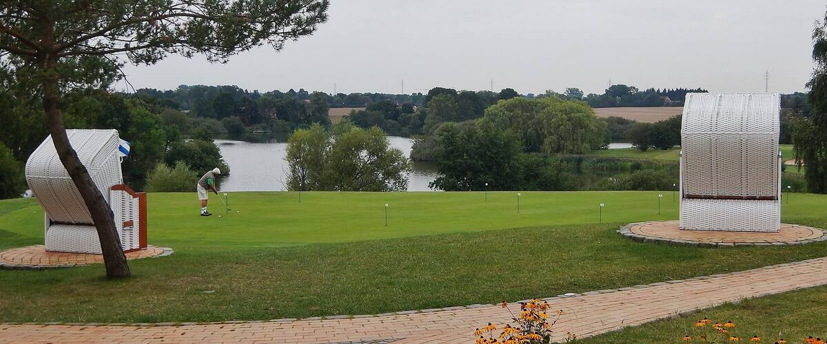 A golf course with a lake, trees, and a sculpture in the foreground.