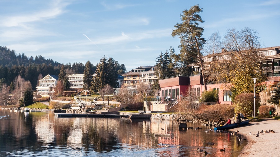 A lake with reflections, a dock, buildings, and a forested hillside.
