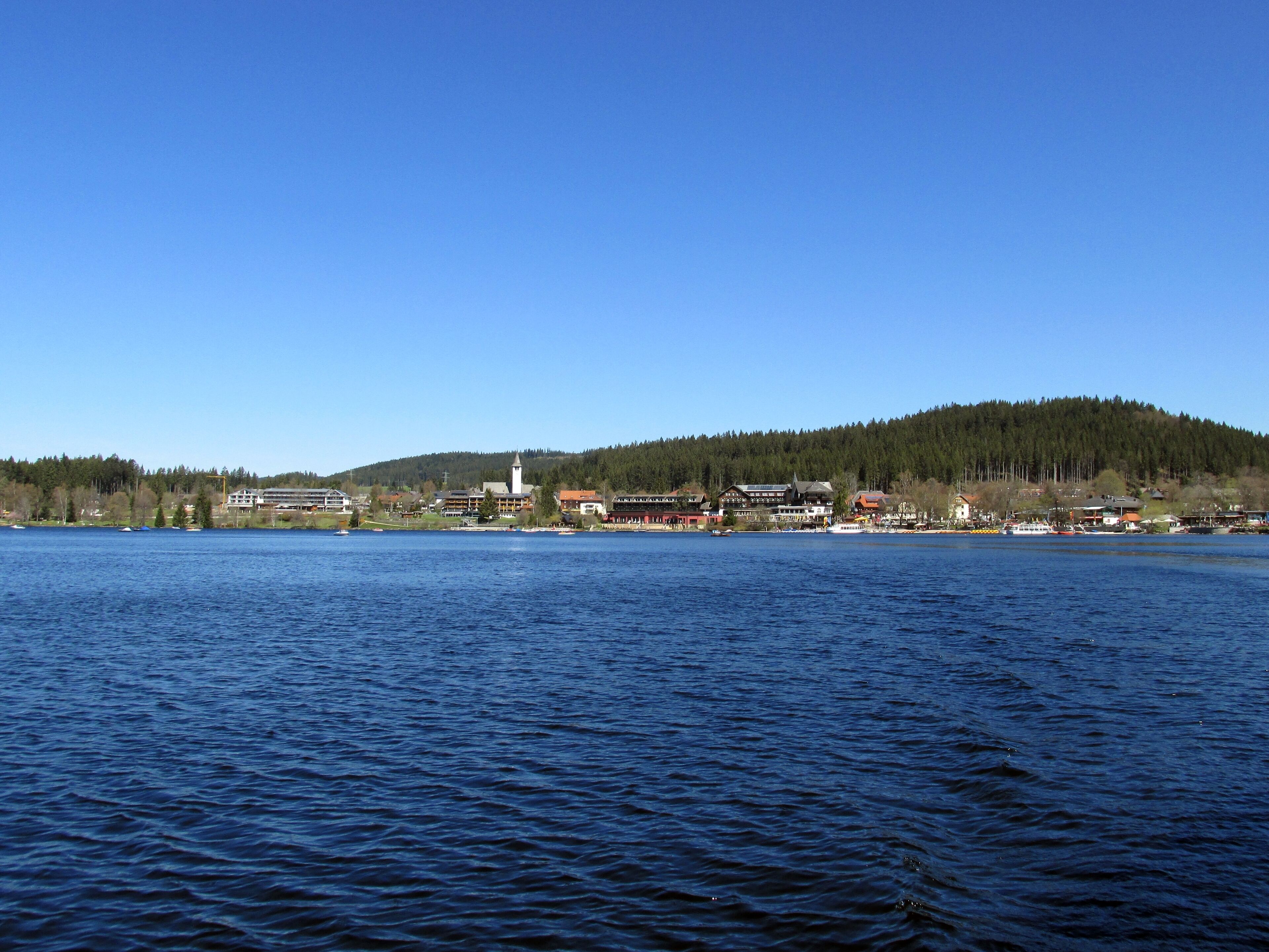 A calm lake with a town on the opposite shore, surrounded by forested hills.
