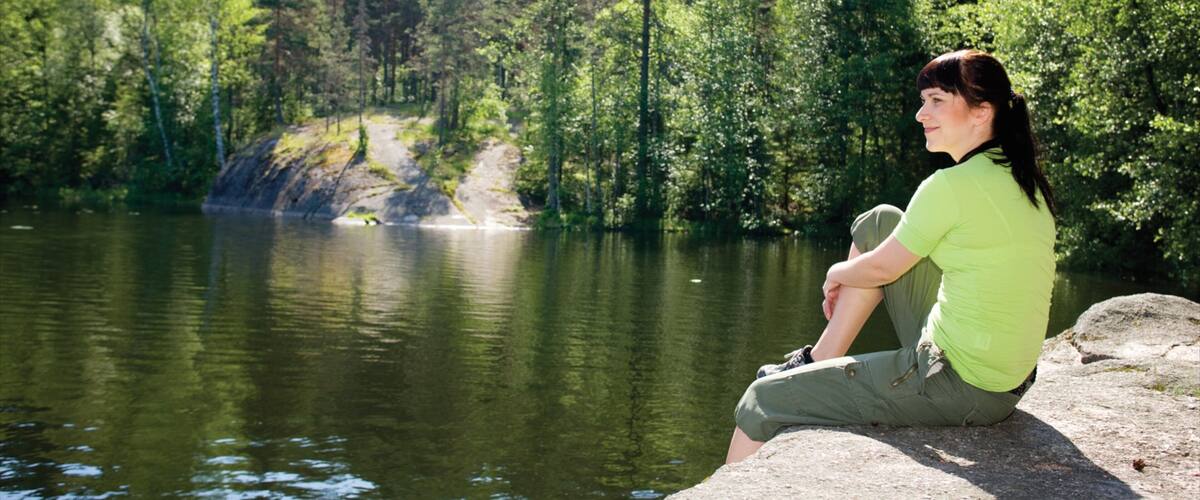 A person sitting on a rock by a calm lake surrounded by dense forest.