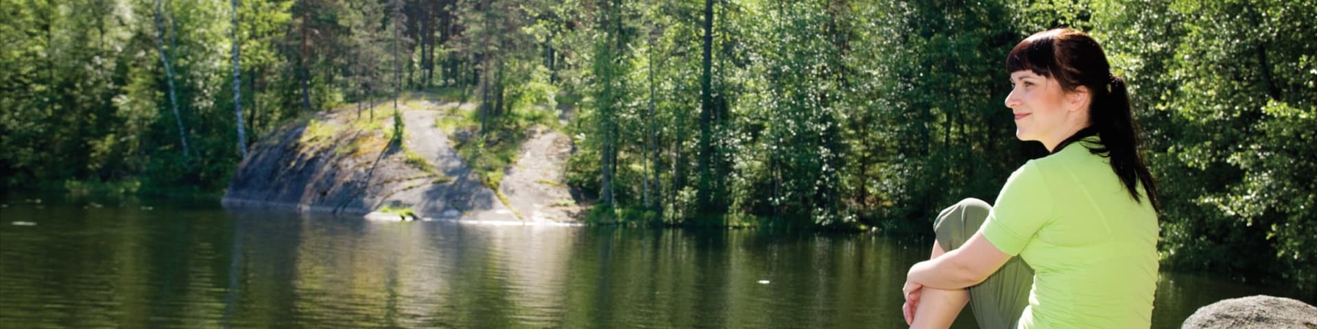 A person sitting on a rock by a calm lake surrounded by dense forest.