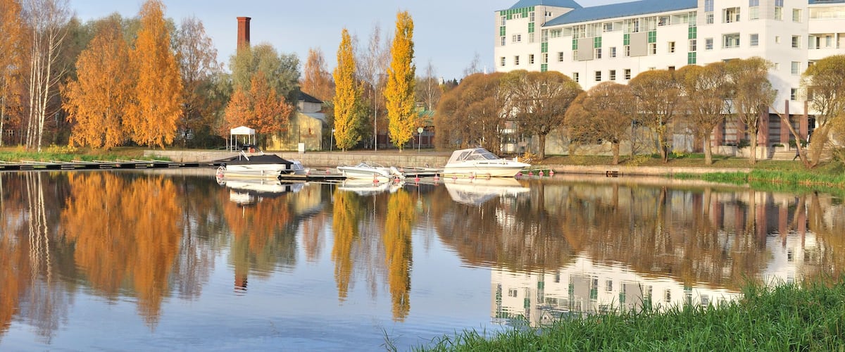 A calm river with boats, autumn trees, and a large building with a green roof.