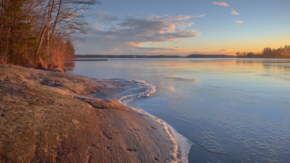 Panorama of the shores of Tuusula lake on a sunny winter day in Jarvenpaa: thin ice stone, sunbeams and bright sky.