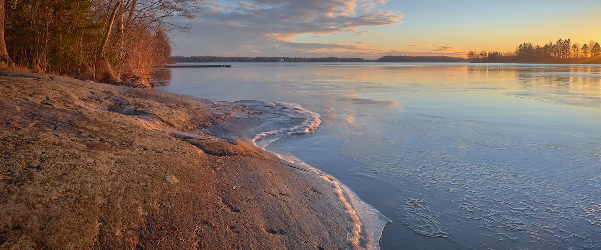 Panorama of the shores of Tuusula lake on a sunny winter day in Jarvenpaa: thin ice stone, sunbeams and bright sky.