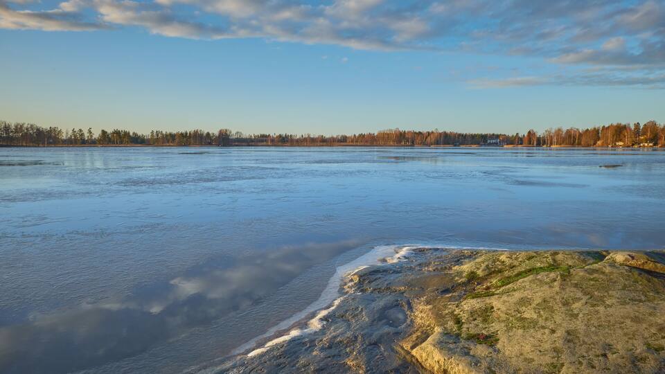 Panorama of the shores of Tuusula lake on a sunny winter day in Järvenpää: thin ice stone, sunbeams and bright sky.