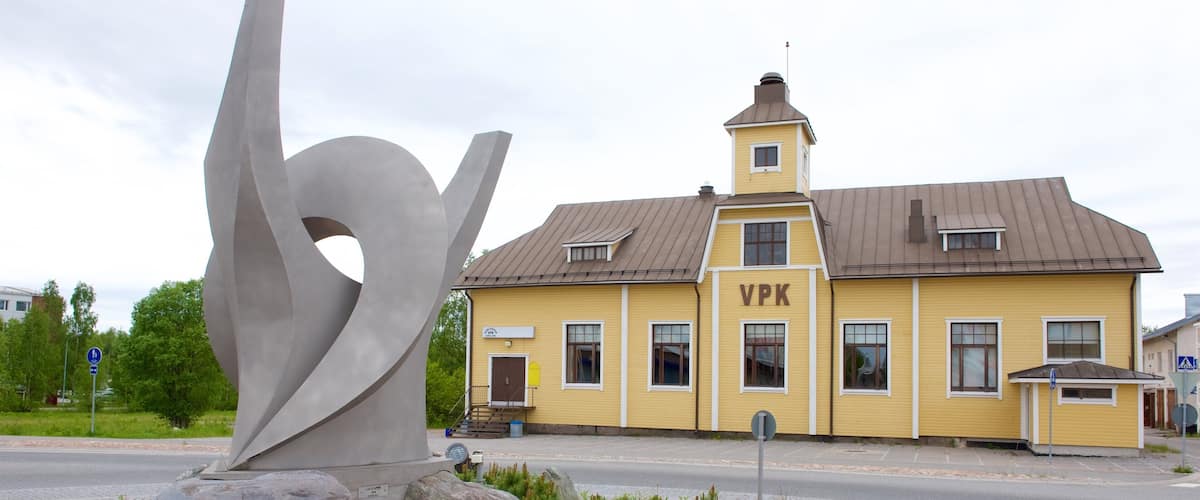 A yellow building with 'VPK' on the side, a large abstract sculpture, and a road with a pedestrian crossing.