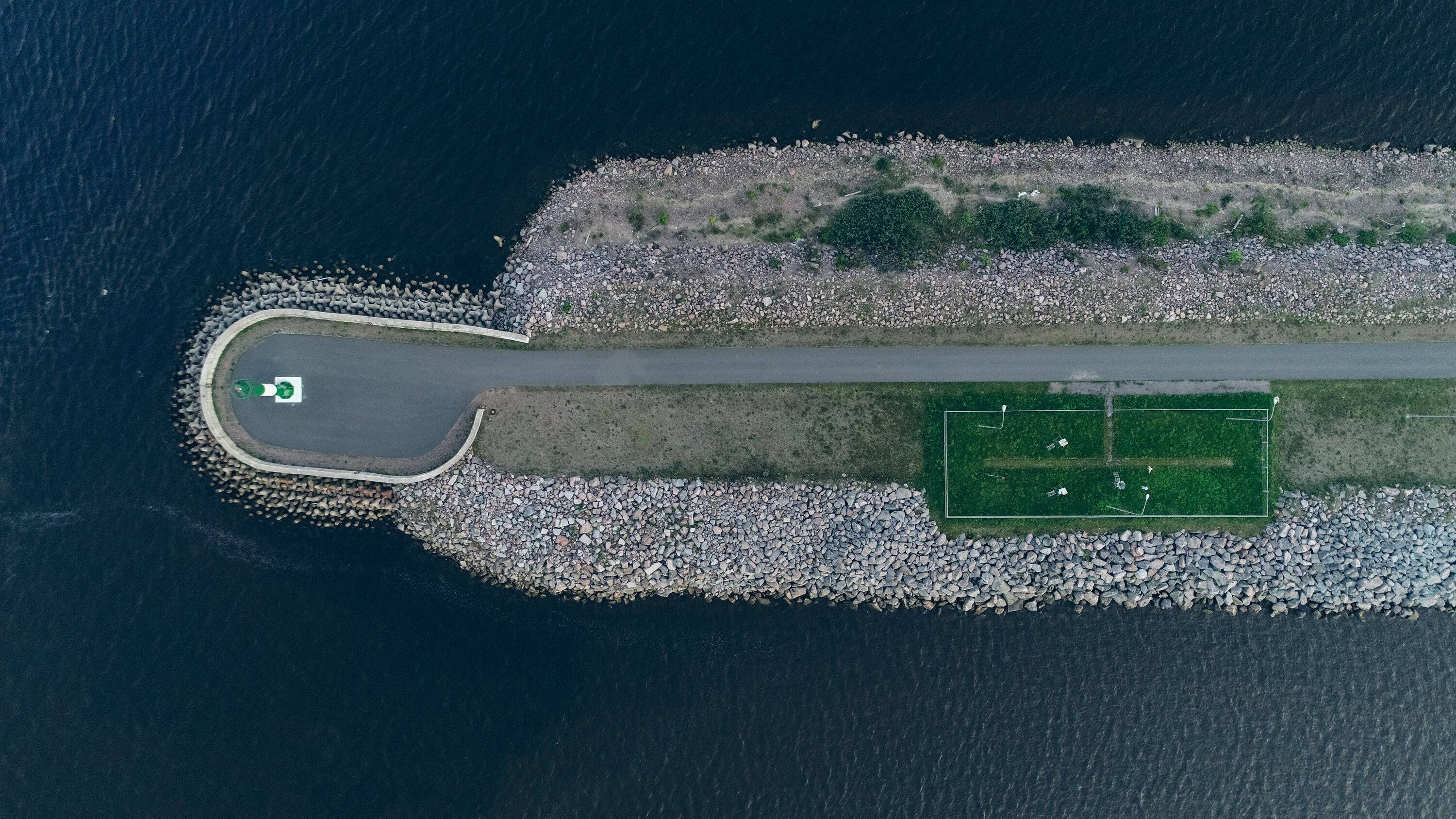 Aerial view of the Lighthouse on the fairway in the Gulf of Finland, navigation is open, summer time. Concrete slabs on the coastline. Breakwaters at the entrance to the port.