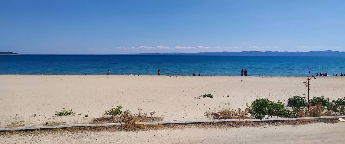 A beach with a clear sky, calm sea, and distant mountains.