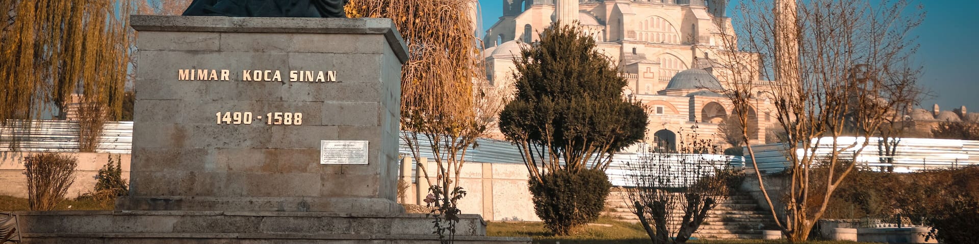 A statue of a historical figure, a mosque with four minarets, and a plaque with a date range.