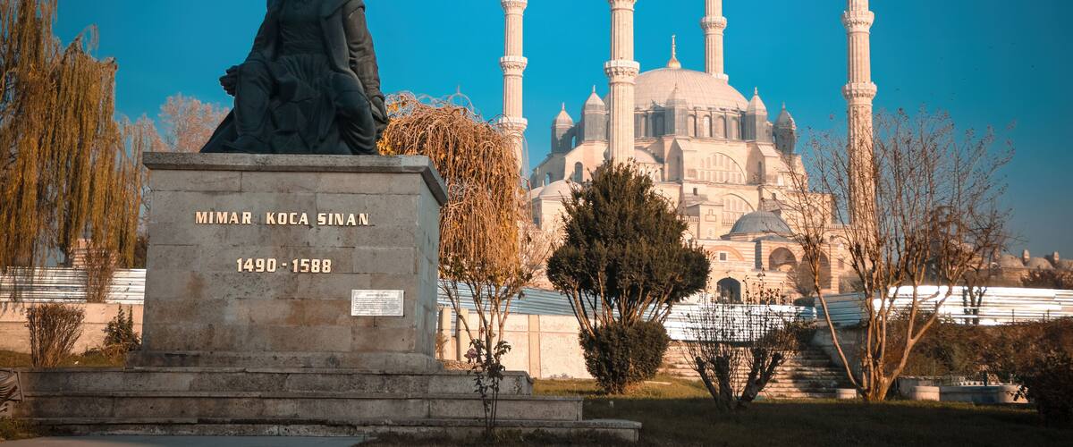 A statue of a historical figure, a mosque with four minarets, and a plaque with a date range.