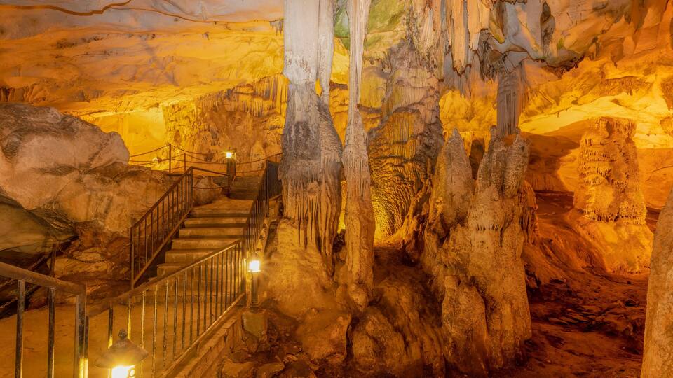 A cave with stalactites, a staircase, and a warm light source.