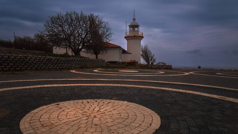 A lighthouse, a brick pathway, and a barren tree.