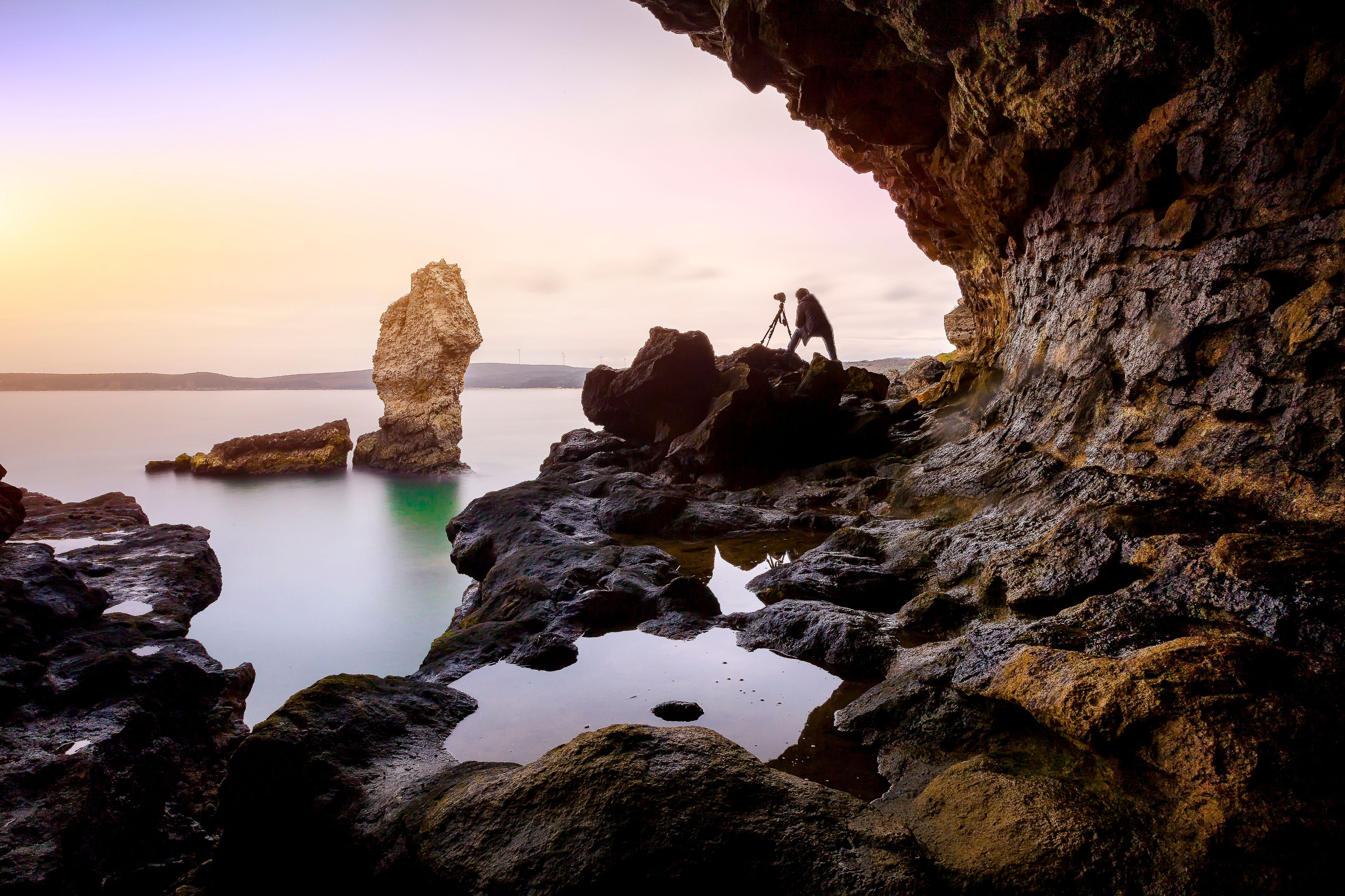 A rocky coastline with a large rock formation and a person with a camera.