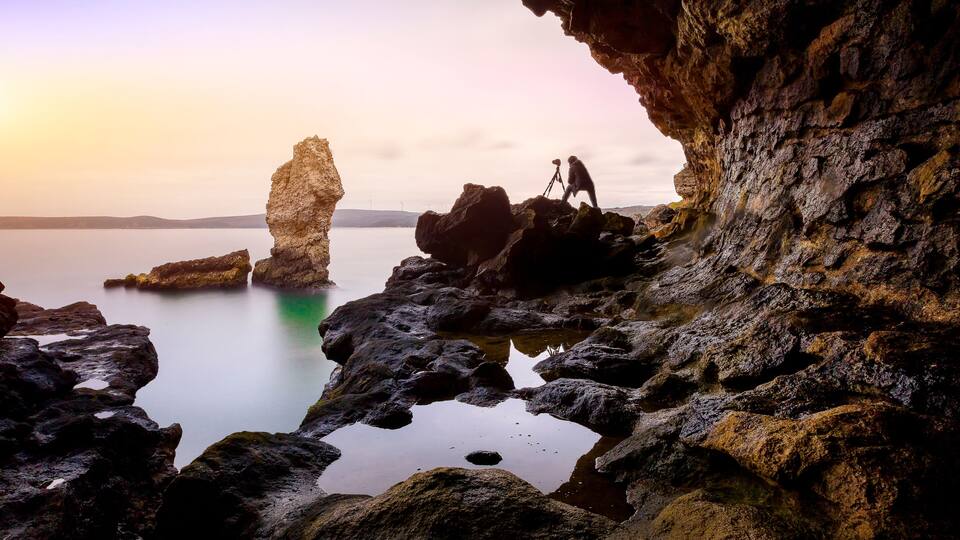 A rocky coastline with a large rock formation and a person with a camera.