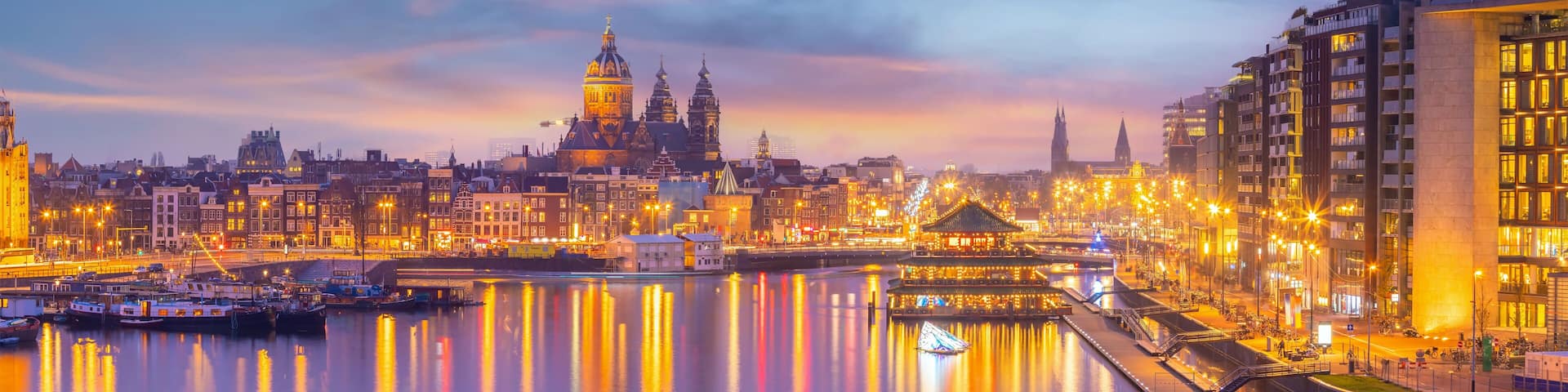 A cityscape at dusk with a prominent cathedral, a river reflecting lights, and modern buildings.